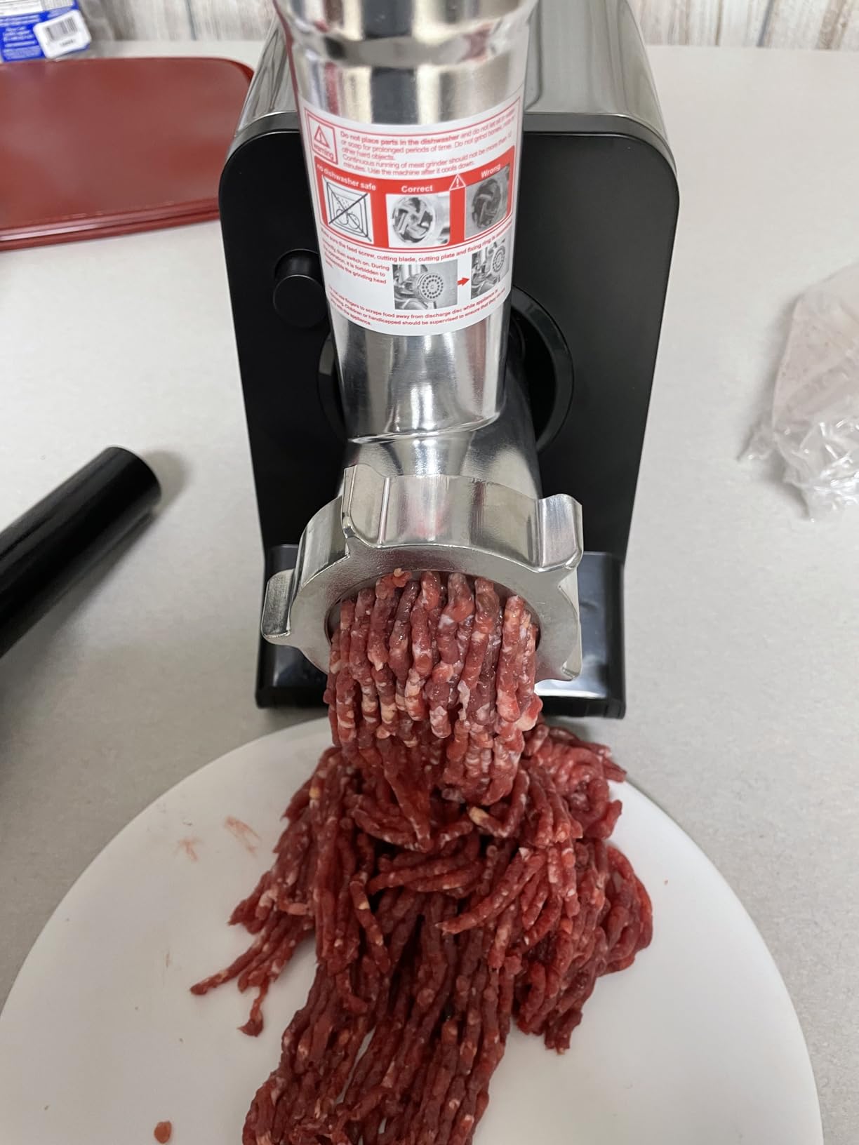 Freshly ground beef coming out of the Altra grinding head onto a white cutting board