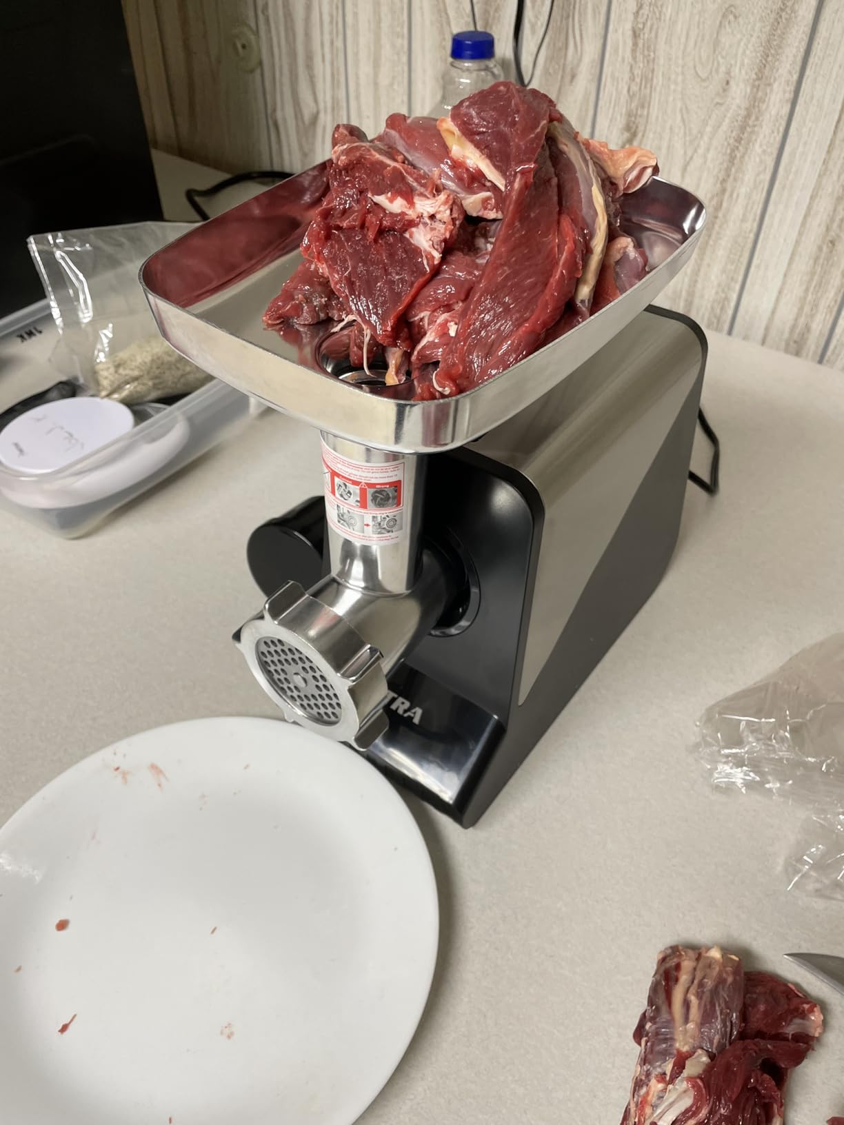 Altra meat grinder with its tray piled high with trimmed red meat, ready to grind, next to an empty white plate