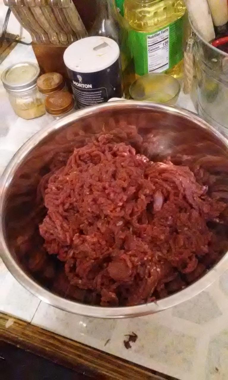 Stainless mixing bowl full of home-ground meat next to spice jars and a salt canister
