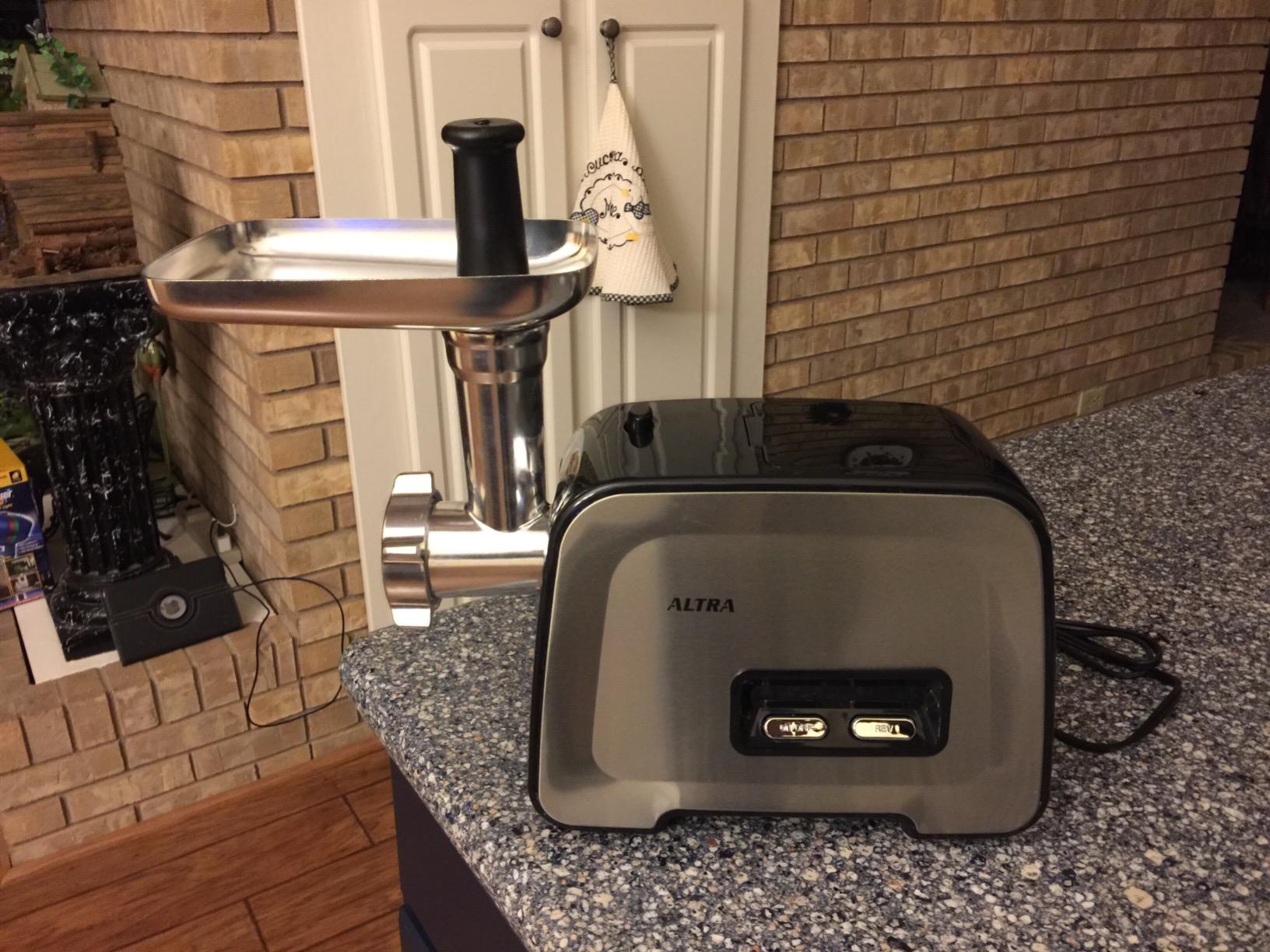 Altra meat grinder set up on a granite counter with the black food pusher standing in the tray